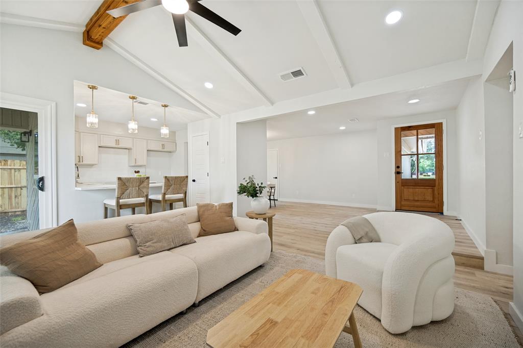Vaulted ceiling living area with a visible kitchen passthrough, wood-finish flooring, recessed lighting, and a prominent wood-panel front door with glass inserts