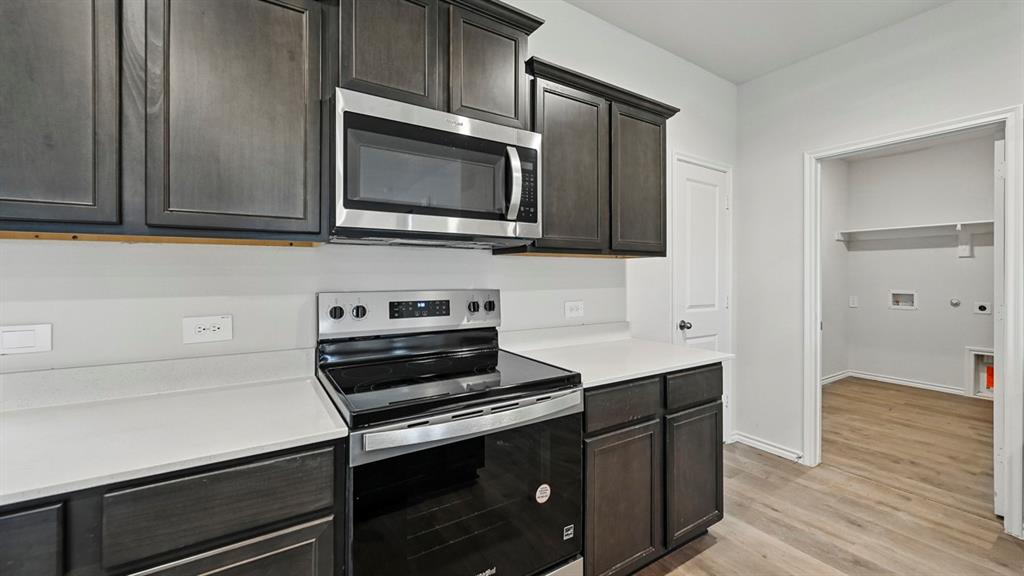 Kitchen workspace featuring dark cabinetry, white countertops, stainless steel appliances, and a smooth-top range