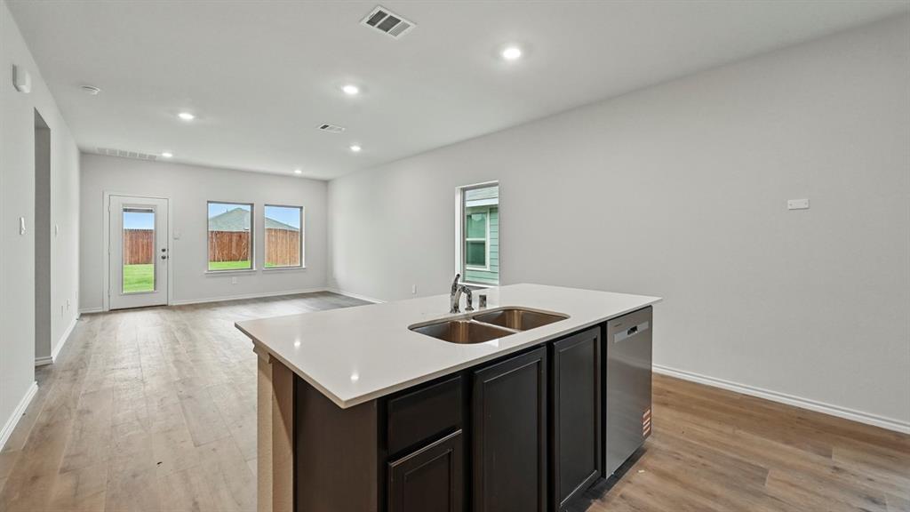 Kitchen island featuring a double-basin stainless steel sink, integrated dishwasher, and light-toned solid surface countertop