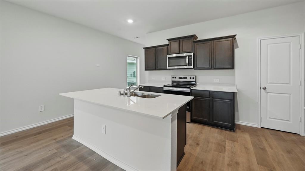 Modern kitchen featuring an island with an undermount sink, dark wood cabinetry, stainless steel appliances, and wood-finish flooring