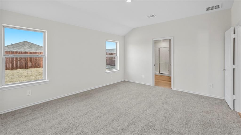 Spacious room featuring vaulted ceilings, light gray carpeting, two windows, and a doorway leading to a bathroom with wood-finish flooring