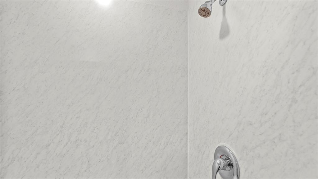 Shower enclosure featuring light-toned, textured wall panels and chrome fixtures including a showerhead and single-handle control