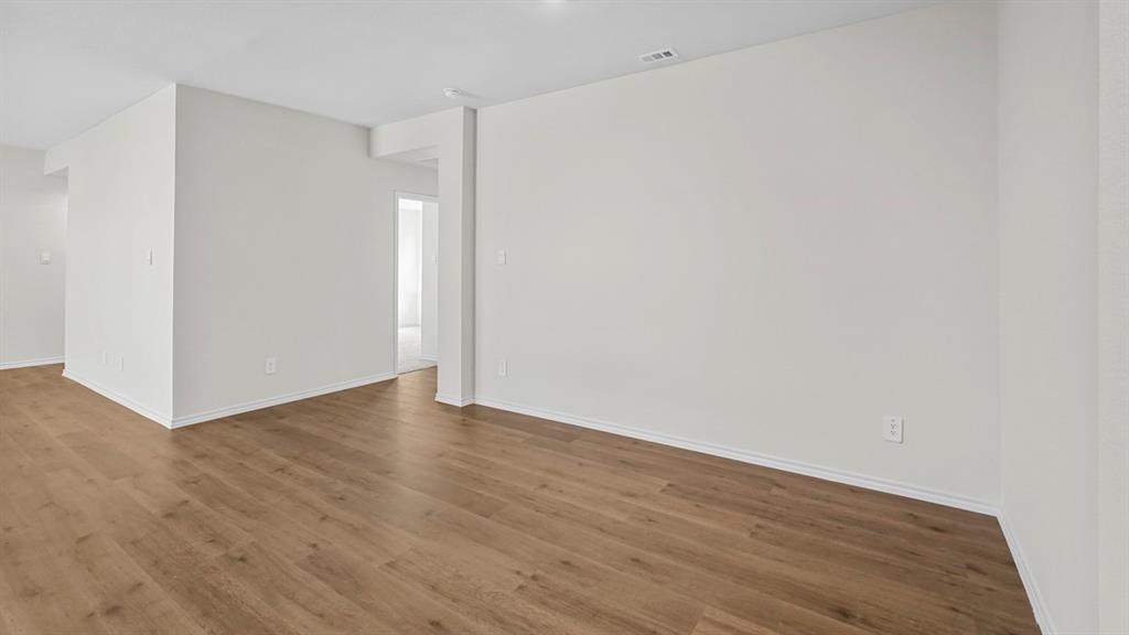 Spacious room featuring wood-finish flooring, white baseboards, recessed lighting, and bright white walls