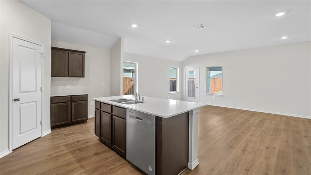 Open-concept kitchen featuring a central island with an undermount sink and dishwasher, wood-finish flooring, recessed lighting, white countertops, and dark wood cabinetry
