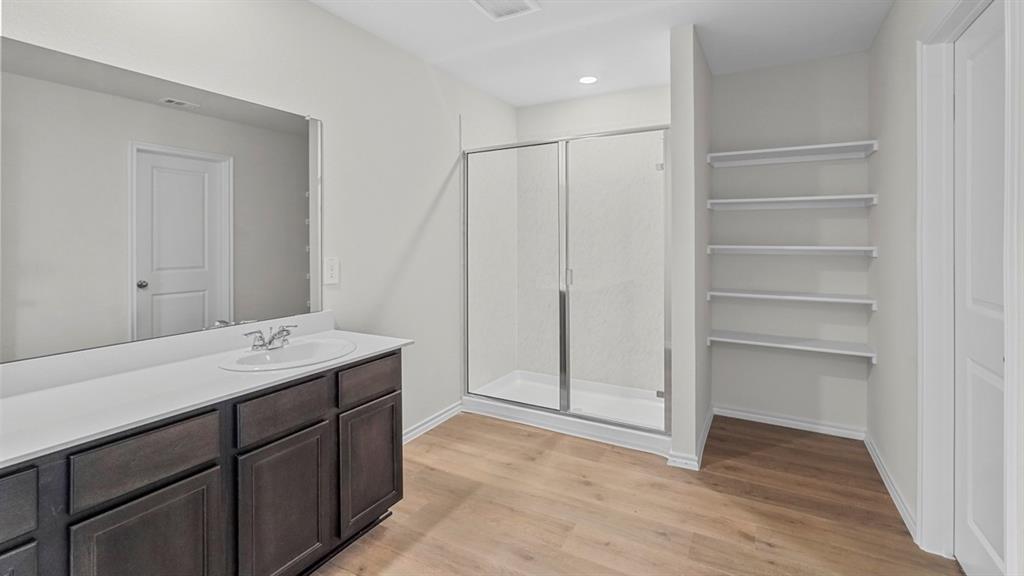 Bathroom featuring a dark wood-finish vanity with an integrated sink, a large wall-mounted mirror, a glass-enclosed shower, built-in shelving, and wood-finish flooring