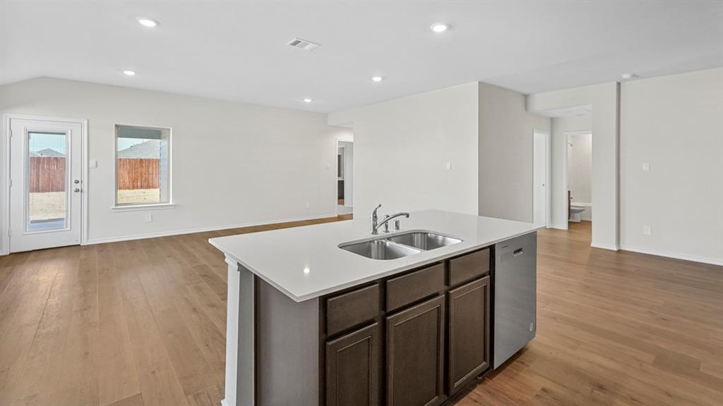 Kitchen island featuring a double-basin stainless steel sink with a high-arc faucet, integrated dishwasher, and white countertop