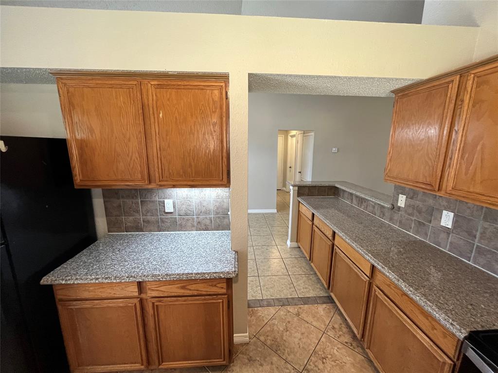 Wood-finish cabinetry, speckled countertops, tile backsplash, and tile flooring Wood-finish cabinetry, speckled countertops, tile backsplash, and tile flooring