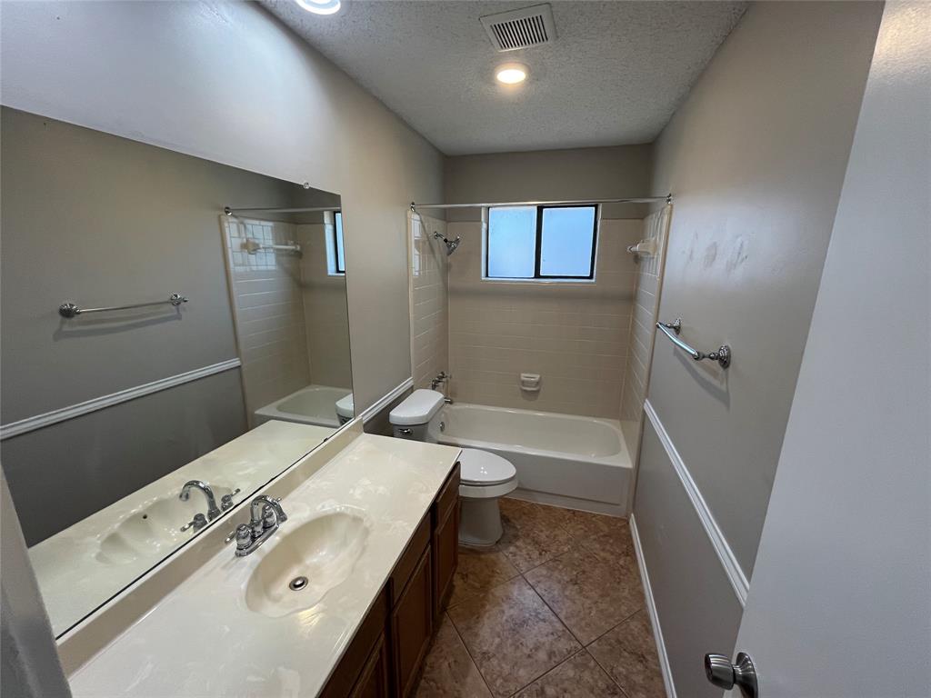 Bathroom featuring a vanity with an integrated sink, a rectangular mirror, a bathtub with a tiled surround, and a fixed window