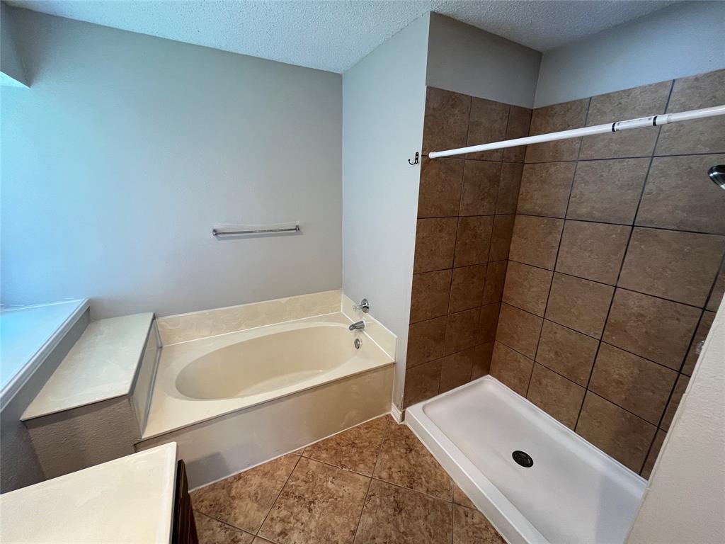 Built-in soaking tub with a tiled surround, separate shower with tiled walls, and coordinating floor tiling