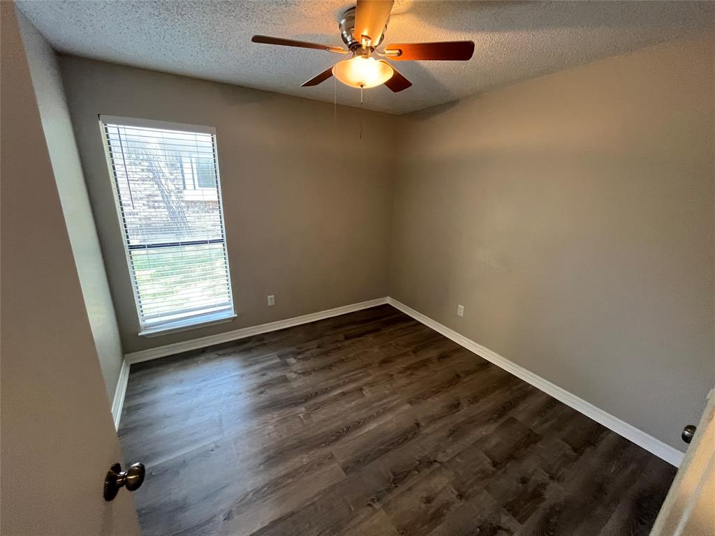 Wood-finish flooring, ceiling fan with integrated lighting, neutral wall tones, and window with blinds