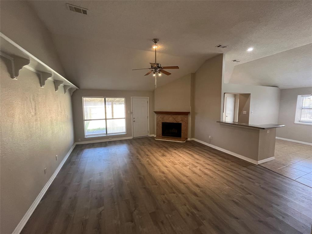 Spacious living area featuring wood-finish flooring, a fireplace with a tile surround and wood mantle, and an integrated breakfast bar with a dark countertop Spacious living area featuring wood-finish flooring, a fireplace with a tile surround and wood mantle, and an integrated breakfast bar with a dark countertop