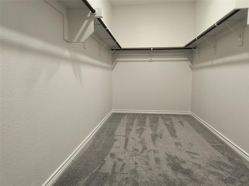 Walk-in closet featuring light gray carpeting, white baseboards, and white textured walls