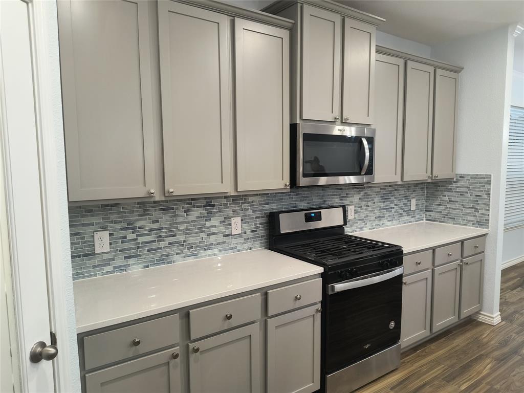 Kitchen featuring wood-finish flooring, a central island, grey cabinetry, a mosaic tile backsplash, and stainless steel appliances including a microwave and range
