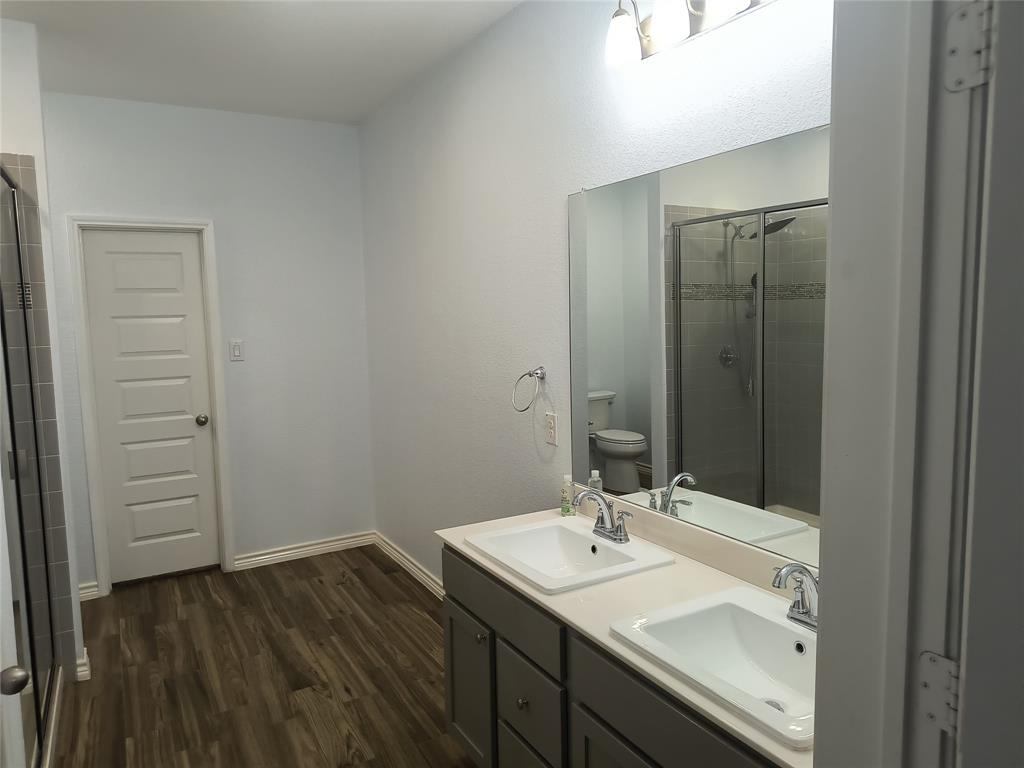 Double vanity with integrated sinks, wood-finish flooring, a frameless mirror, and a glass-enclosed shower with tiled walls