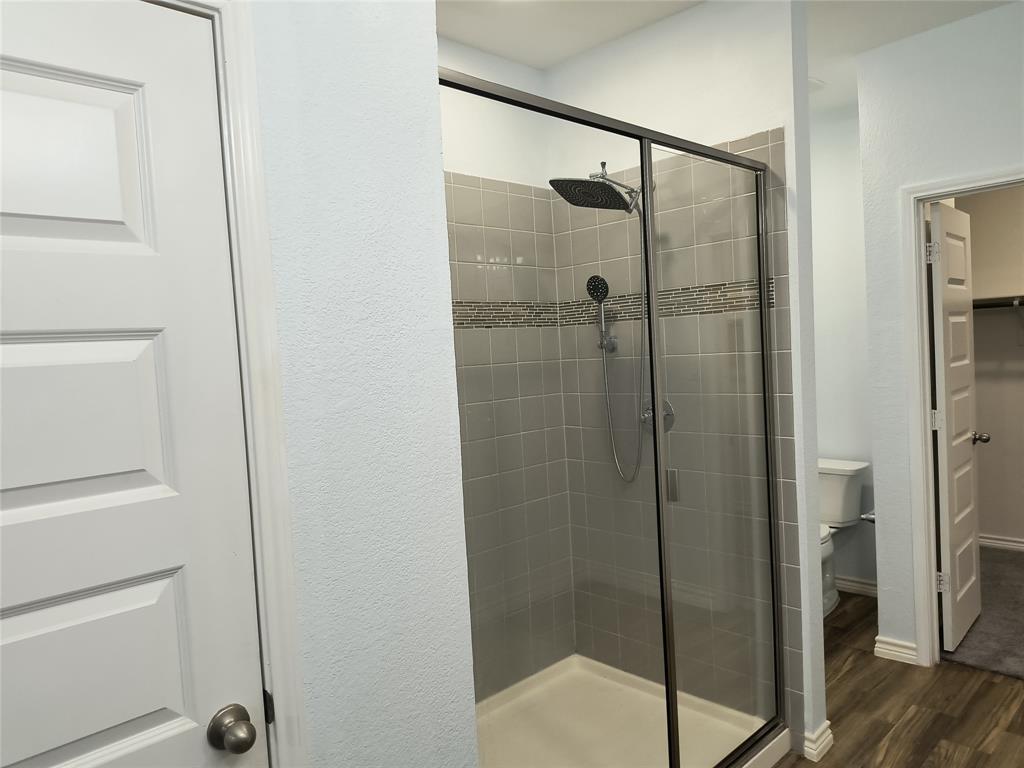 Glass-enclosed shower featuring a rainfall showerhead, handheld sprayer, and tiled walls with a decorative mosaic accent band