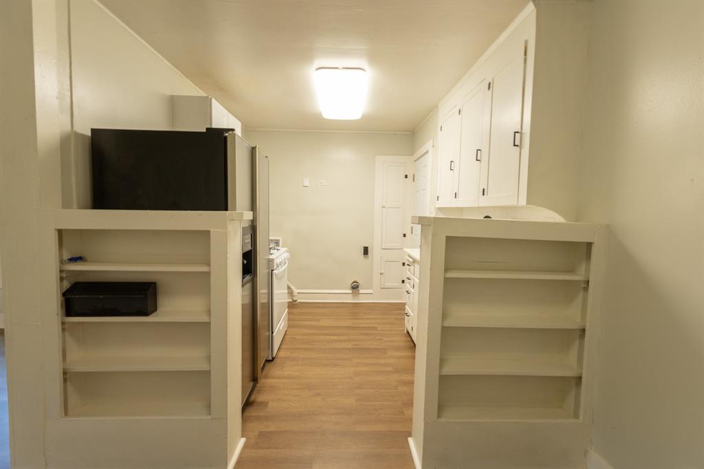 Galley kitchen featuring wood-finish flooring, white built-in shelving, stainless steel refrigerator, white range, and white cabinetry Galley kitchen featuring wood-finish flooring, white built-in shelving, stainless steel refrigerator, white range, and white cabinetry