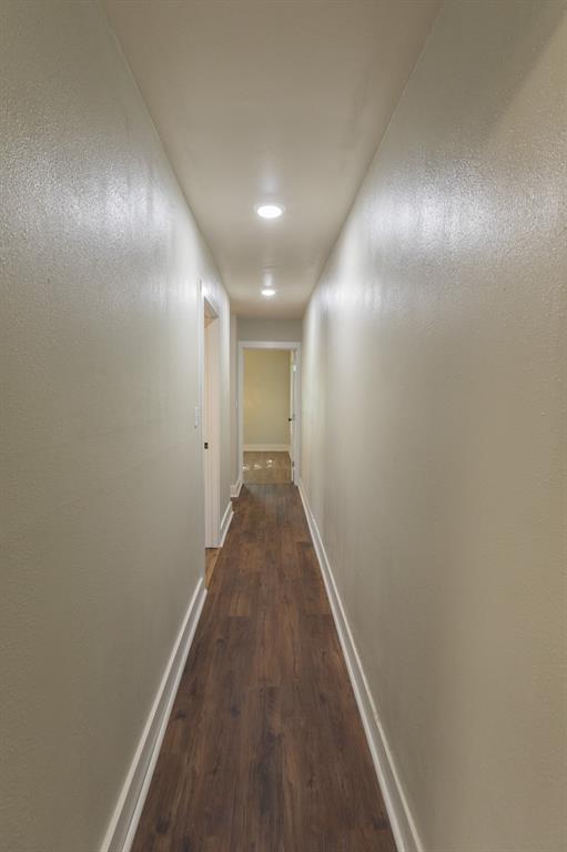Hallway featuring recessed lighting, wood-finish flooring, light neutral wall color, white trim, and a white interior door