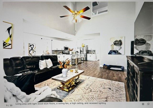 Spacious living area featuring high ceilings, wood-style flooring, a ceiling fan, and recessed lighting