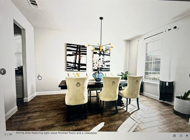 Dining area featuring wood-finish flooring, a modern chandelier, and ample natural light from a large window Dining area featuring wood-finish flooring, a modern chandelier, and ample natural light from a large window