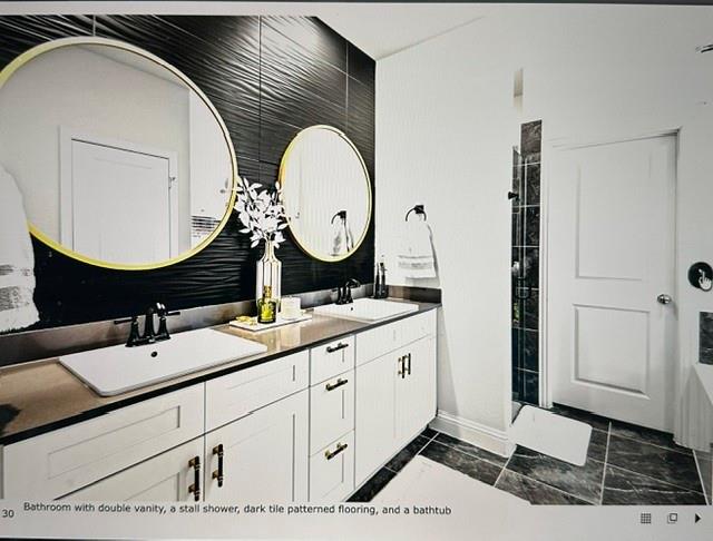 Modern bathroom featuring a double vanity with white cabinetry and dark countertops, accented by two gold-framed circular mirrors