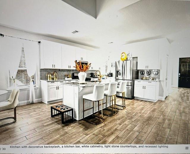 Spacious kitchen featuring wood-finish flooring, white cabinetry, light stone countertops, a decorative backsplash, and recessed lighting Spacious kitchen featuring wood-finish flooring, white cabinetry, light stone countertops, a decorative backsplash, and recessed lighting