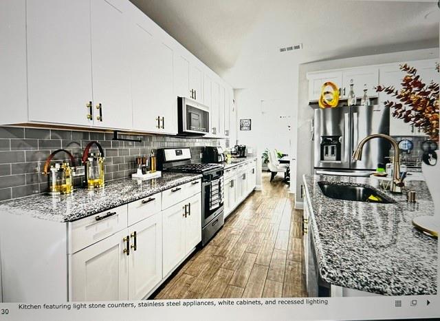 Kitchen featuring white cabinetry, light stone countertops, stainless steel appliances, grey subway tile backsplash, and wood-finish flooring