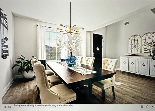 Dining area featuring wood-finish flooring, a contemporary chandelier, a window with white curtains, and light-toned walls Dining area featuring wood-finish flooring, a contemporary chandelier, a window with white curtains, and light-toned walls