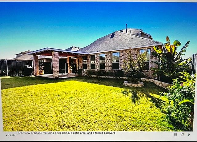 Spacious backyard featuring a covered patio, brick siding, a manicured lawn, and perimeter fencing