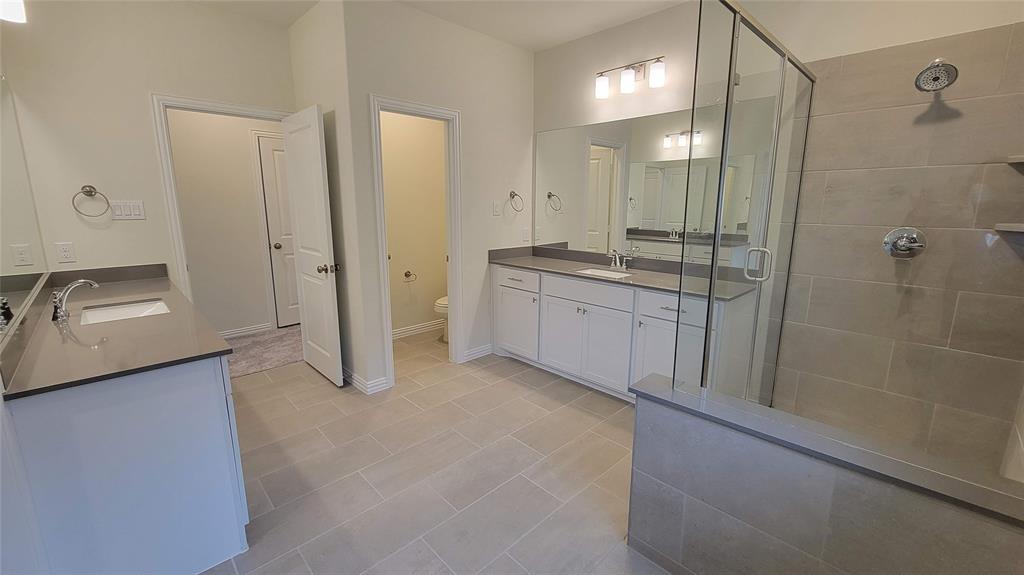 Spacious bathroom featuring dual vanities with integrated sinks and dark countertops, a glass-enclosed shower with tile surround, and light-toned tile flooring