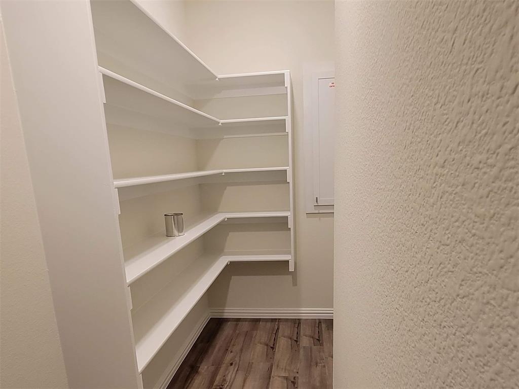 Spacious pantry featuring extensive white shelving, a natural wood-finish floor, and light-toned walls