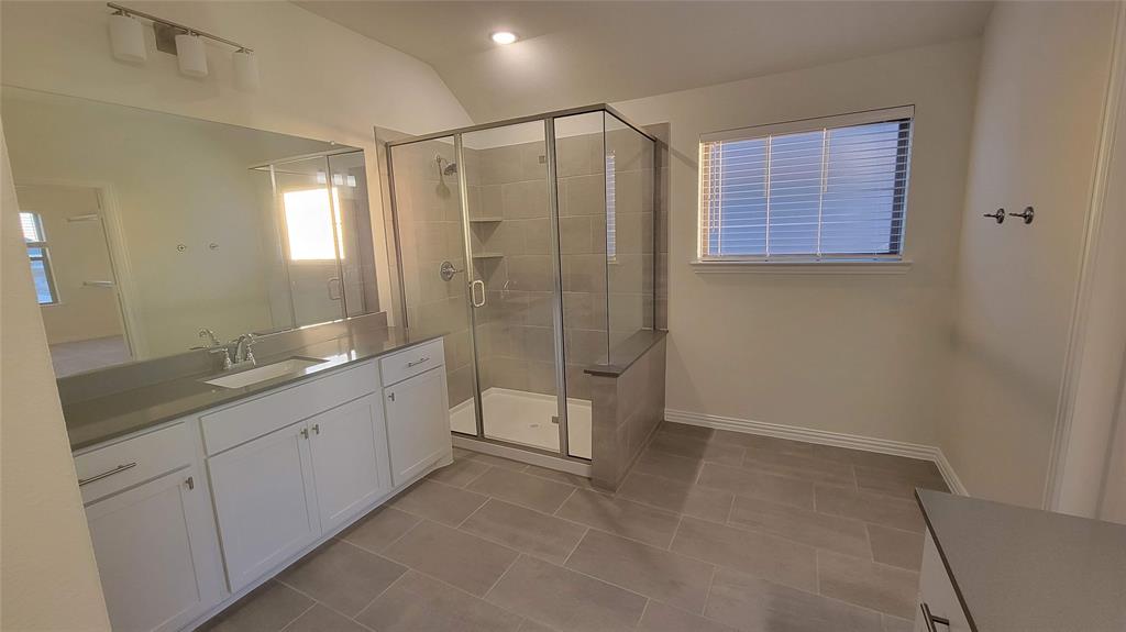 Bathroom featuring a glass-enclosed shower with a built-in bench, a spacious vanity with a single basin sink and stone countertop, white shaker-style cabinetry, and large format tile flooring