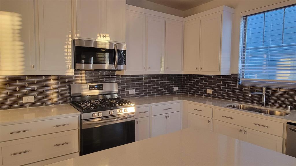 Modern kitchen featuring white shaker cabinetry, stainless steel appliances, a subway tile backsplash, and light-toned countertops