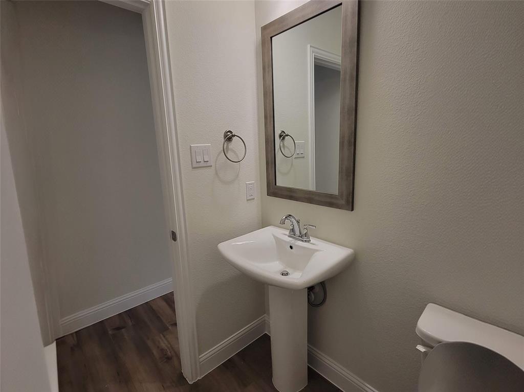 Pedestal sink with chrome faucet, framed mirror, and wood-finish flooring