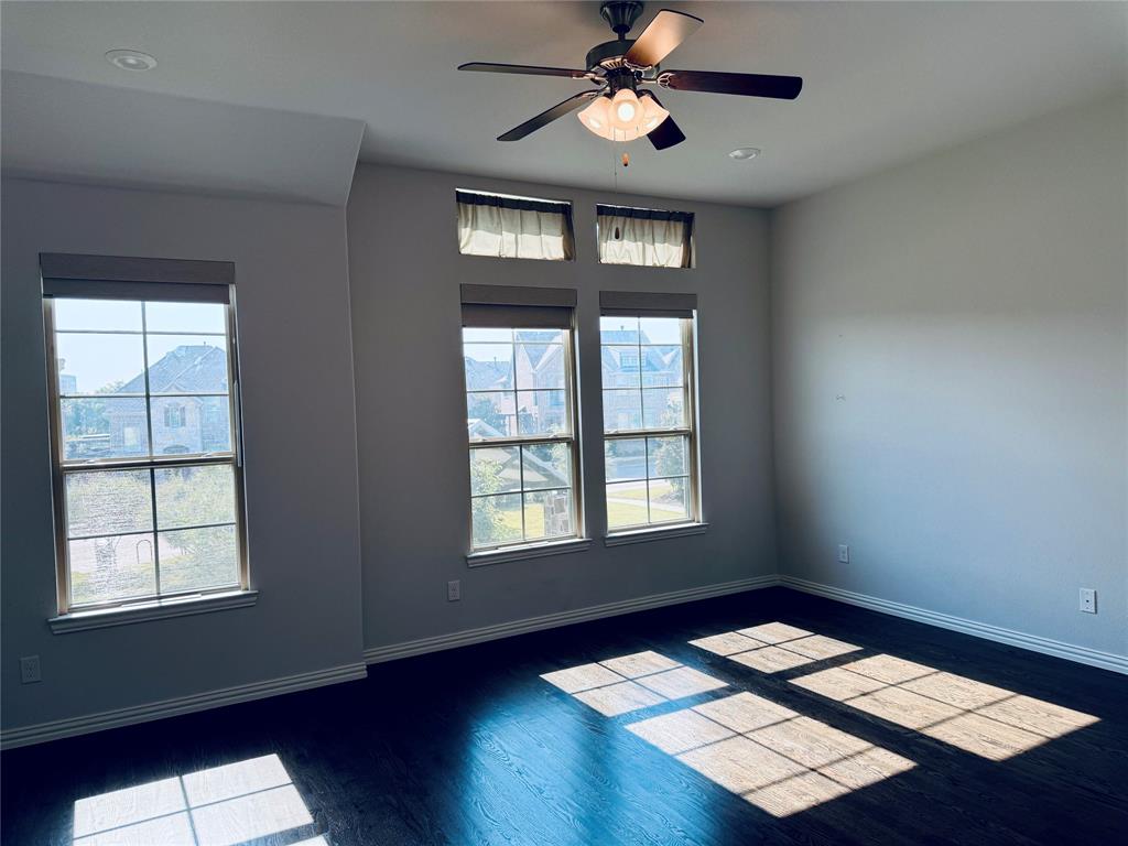 Spacious room featuring multiple windows, wood-finish flooring, a ceiling fan with integrated lighting with motorized blinds
