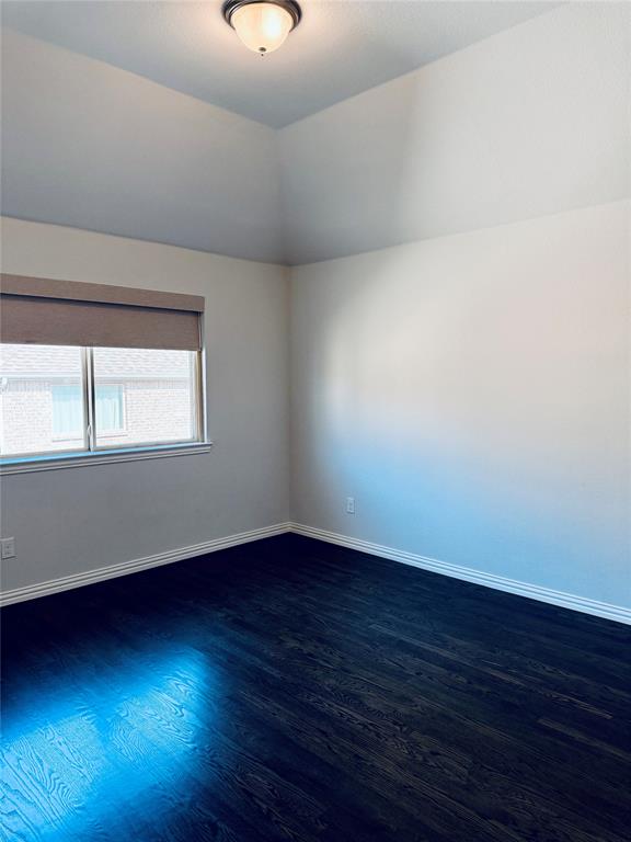 2nd Spacious bedroom featuring dark wood-finish flooring, crisp white walls, and a recessed window with a neutral roller shade
