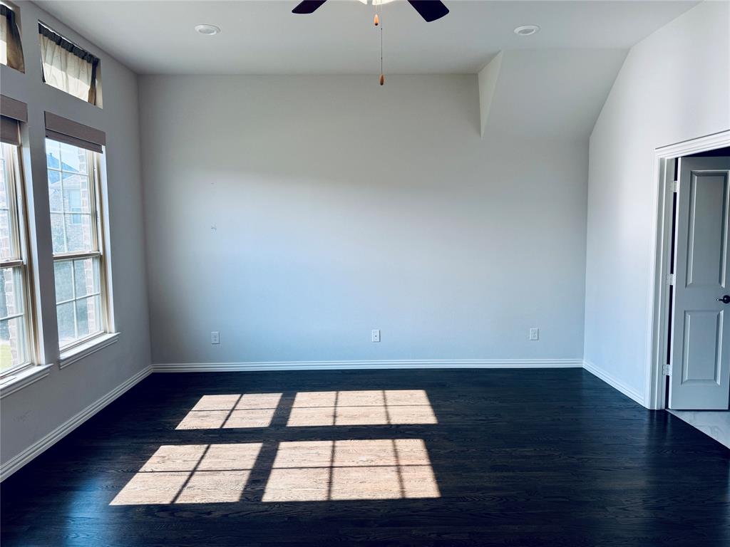 Spacious room featuring dark wood-finish flooring, white walls, and a vaulted ceiling