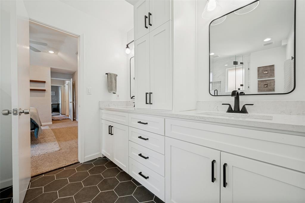 Bathroom featuring a dual vanity with white cabinetry and black hardware