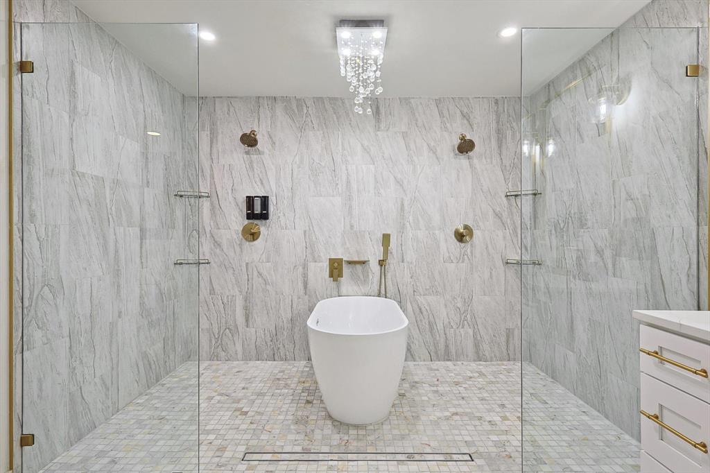 Freestanding soaking tub centered within a spacious wet room featuring two glass-enclosed shower areas
