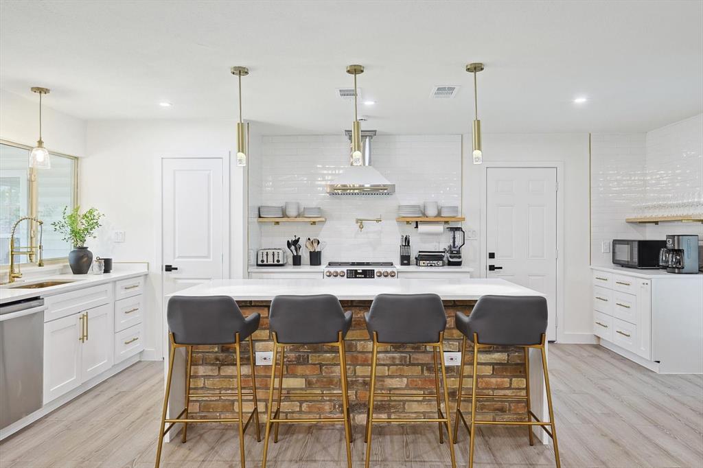 Modern kitchen featuring a brick-clad island with seating, white shaker cabinetry, stainless steel appliances, white subway tile backsplash, and light wood-finish flooring Modern kitchen featuring a brick-clad island with seating, white shaker cabinetry, stainless steel appliances, white subway tile backsplash, and light wood-finish flooring