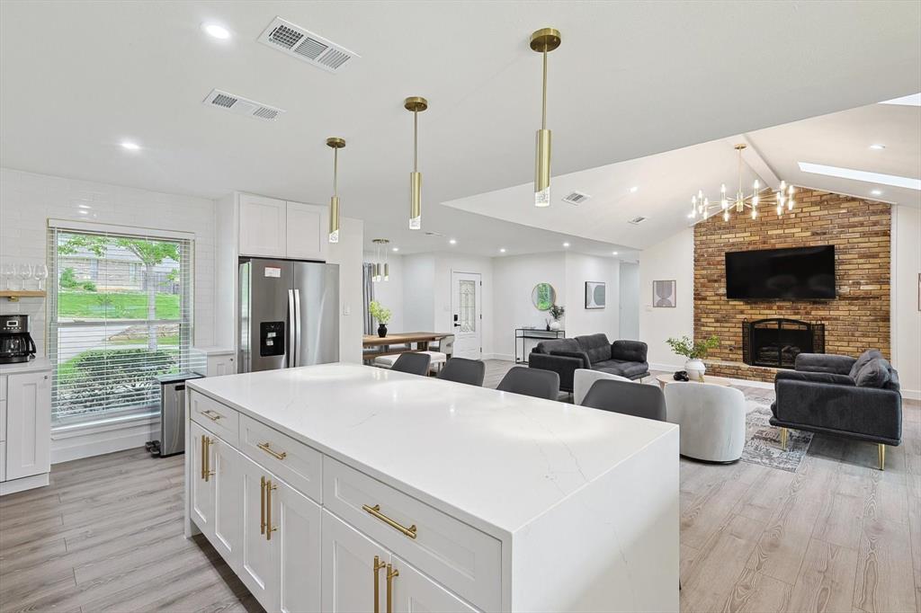 Open-concept kitchen featuring a large central island with white cabinetry and brass hardware, complemented by light wood-finish flooring