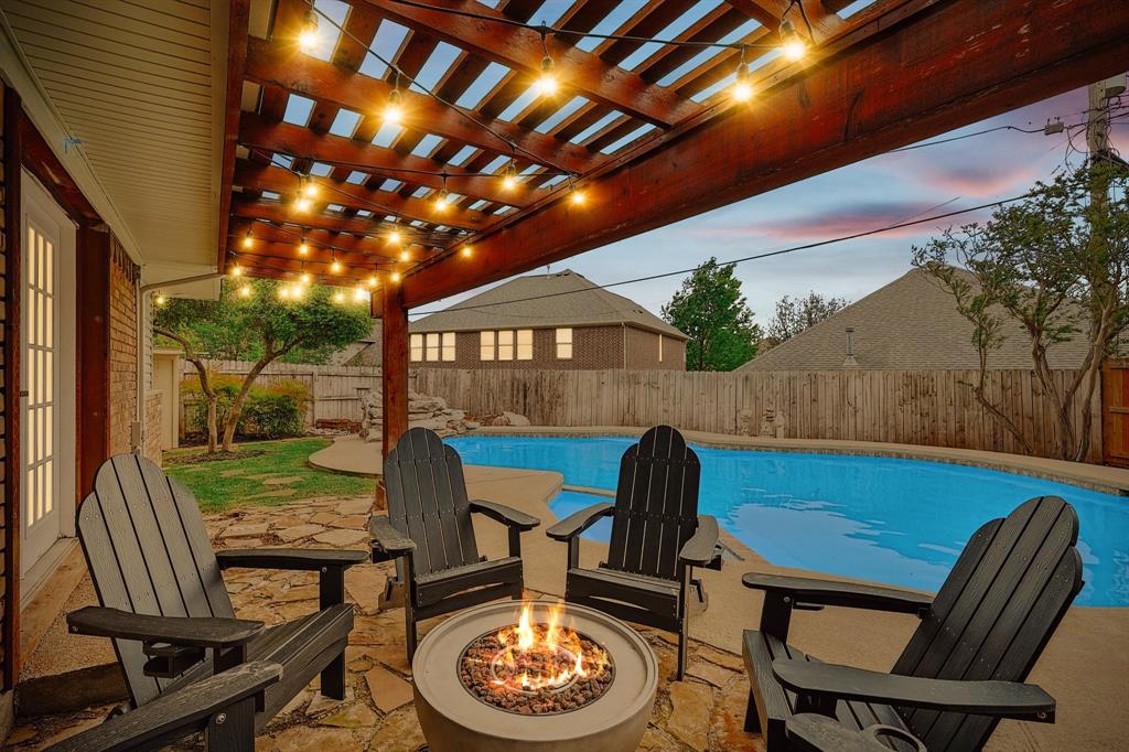 Outdoor living area featuring a wood pergola with string lights, a stone patio, an in-ground swimming pool, and a fire pit