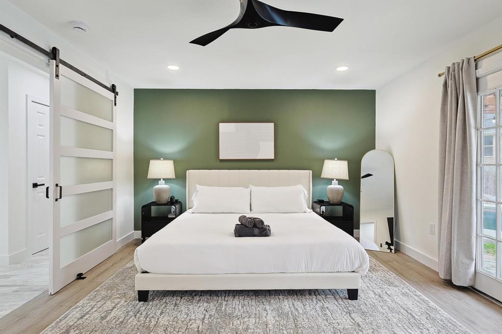 Bedroom featuring a dark green accent wall, wood-finish flooring, a modern barn door with frosted glass panels, recessed lighting, and a black ceiling fan