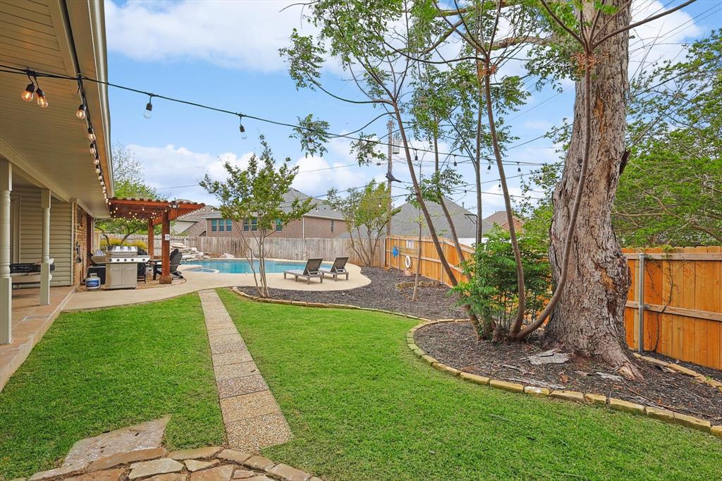 Expansive backyard featuring a stone pathway, mature trees, and a wooden pergola covering a built-in outdoor kitchen