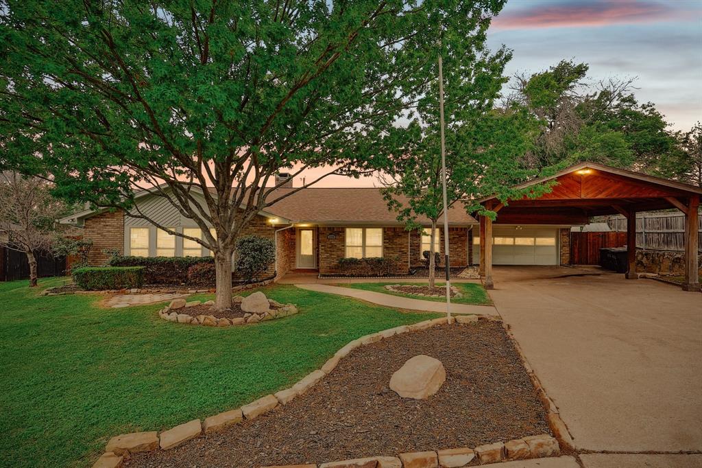 Brick exterior featuring a covered carport, two-car garage, and established landscaping Brick exterior featuring a covered carport, two-car garage, and established landscaping