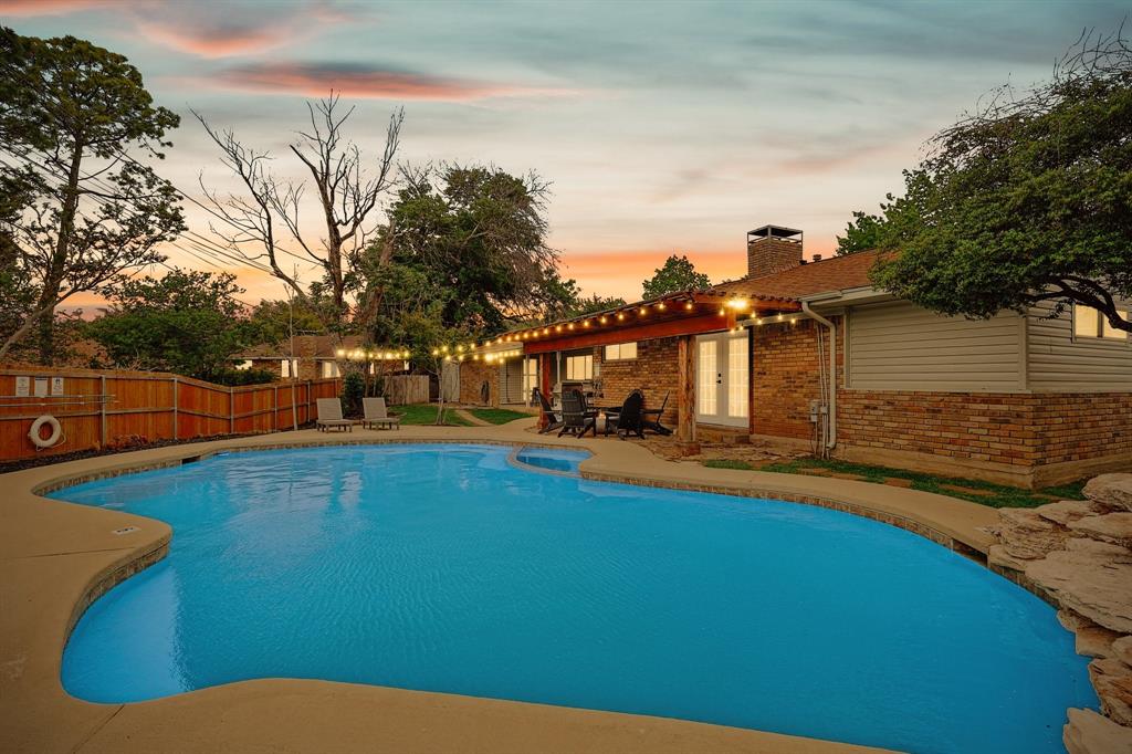 Resort-style backyard featuring a freeform swimming pool, concrete patio, and a brick exterior with white French doors