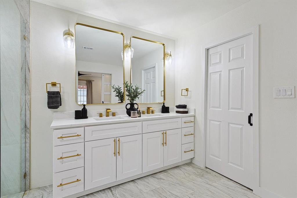 White dual vanity with quartz countertop, dual gold-framed mirrors, gold-finish hardware, and a six-panel door