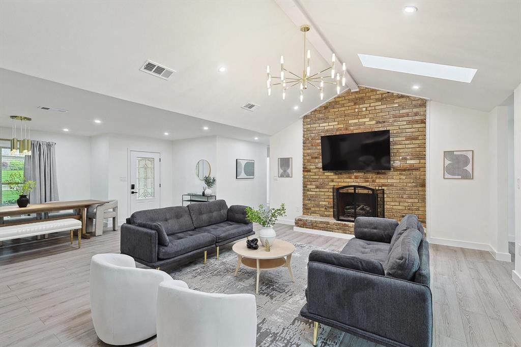 Vaulted ceiling living area featuring a brick fireplace surround, wood-finish flooring, recessed lighting, and a skylight Vaulted ceiling living area featuring a brick fireplace surround, wood-finish flooring, recessed lighting, and a skylight