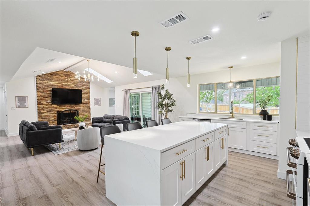Open-concept living area featuring wood-finish flooring, a brick fireplace, and a kitchen island with a quartz countertop