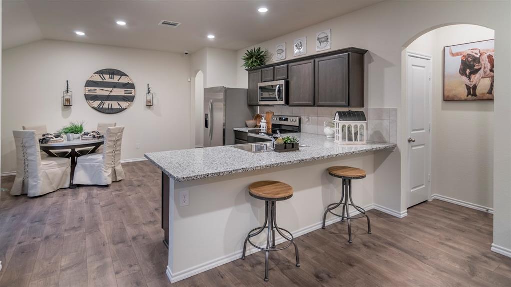 Open-concept interior featuring wood-finish flooring, a kitchen island with stone countertops and a breakfast bar, and dark wood cabinetry with stainless steel appliances
