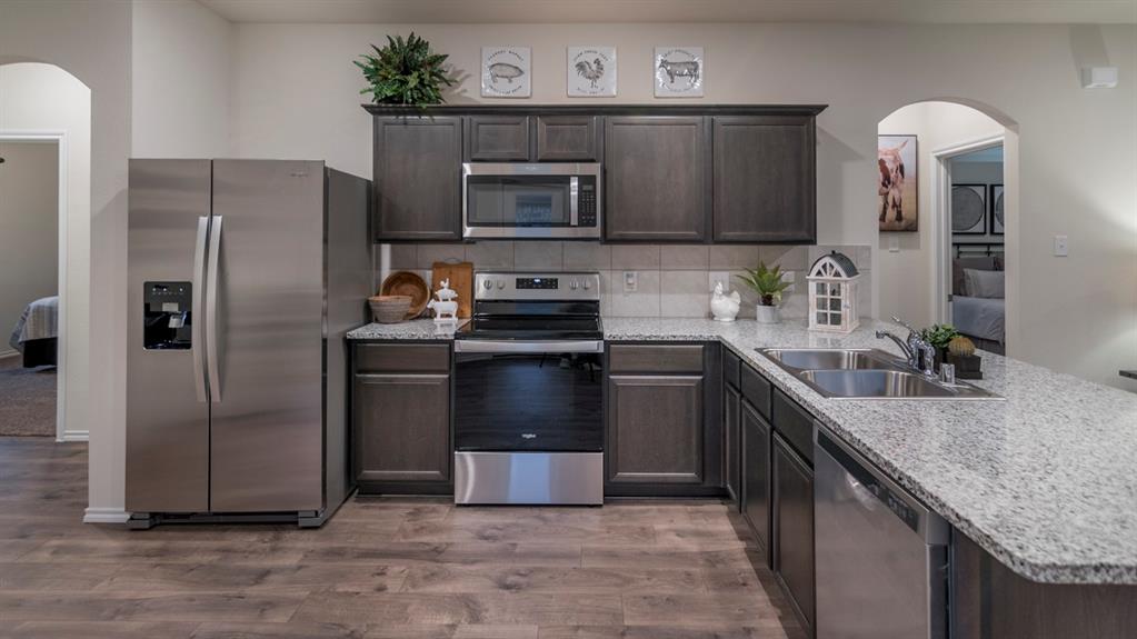 Well-appointed kitchen featuring wood-finish flooring, dark wood cabinetry, stainless steel appliances, and light-toned speckled countertops with a tile backsplash
